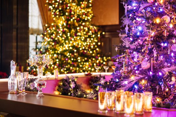 An octagonal bar with blown glass drinkware on top among decorated Christmas trees.